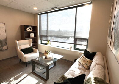 Spacious therapy room at Journey Psychology with sofa, armchair, coffee table, and large window.